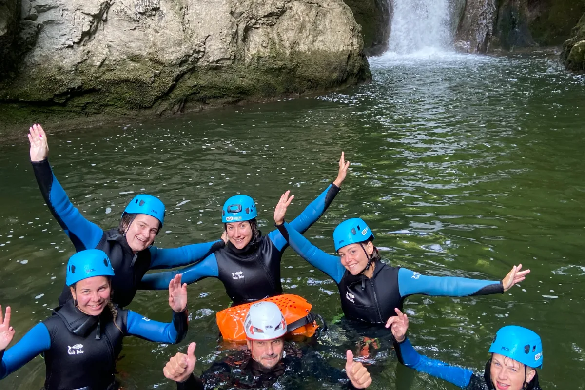 Groupe d'amis souriants dans une vasque au pied d'une cascade pendant une sortie canyoning dans le Jura