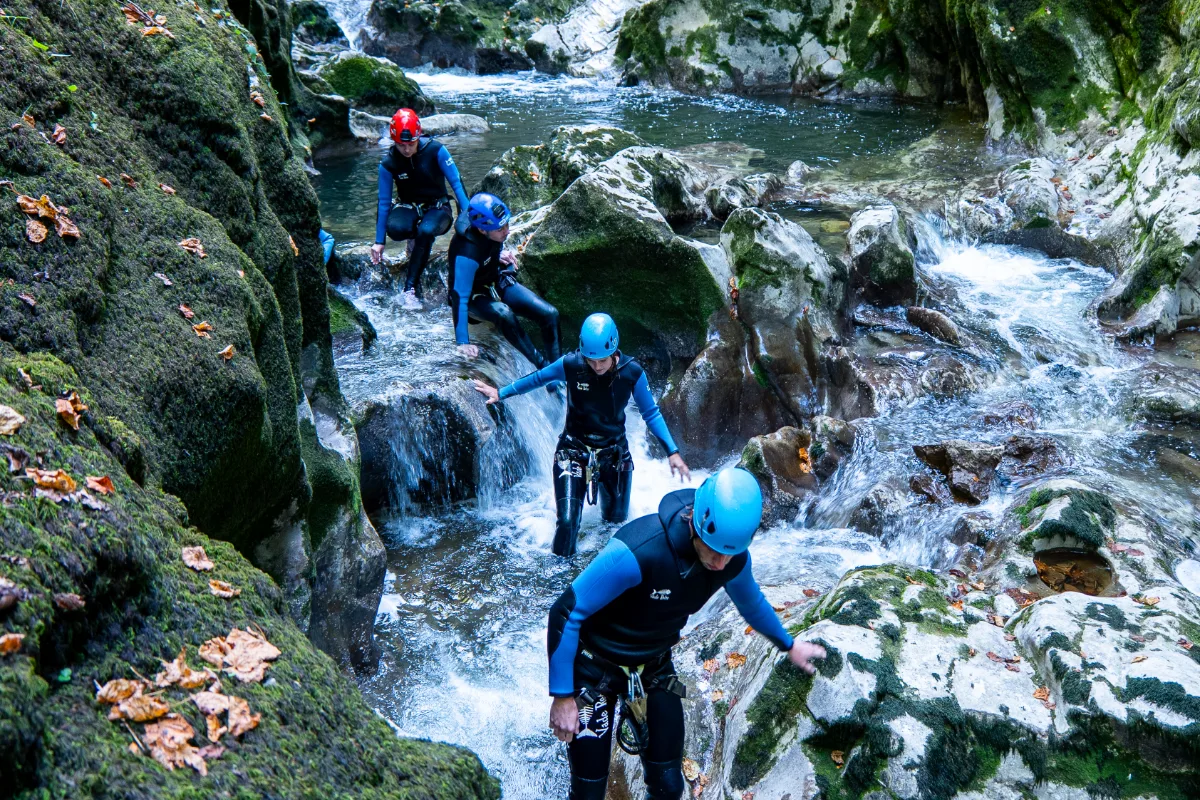 Canyonistes descendant une rivière entre des rochers moussus couverts de feuilles mortes dans le Jura
