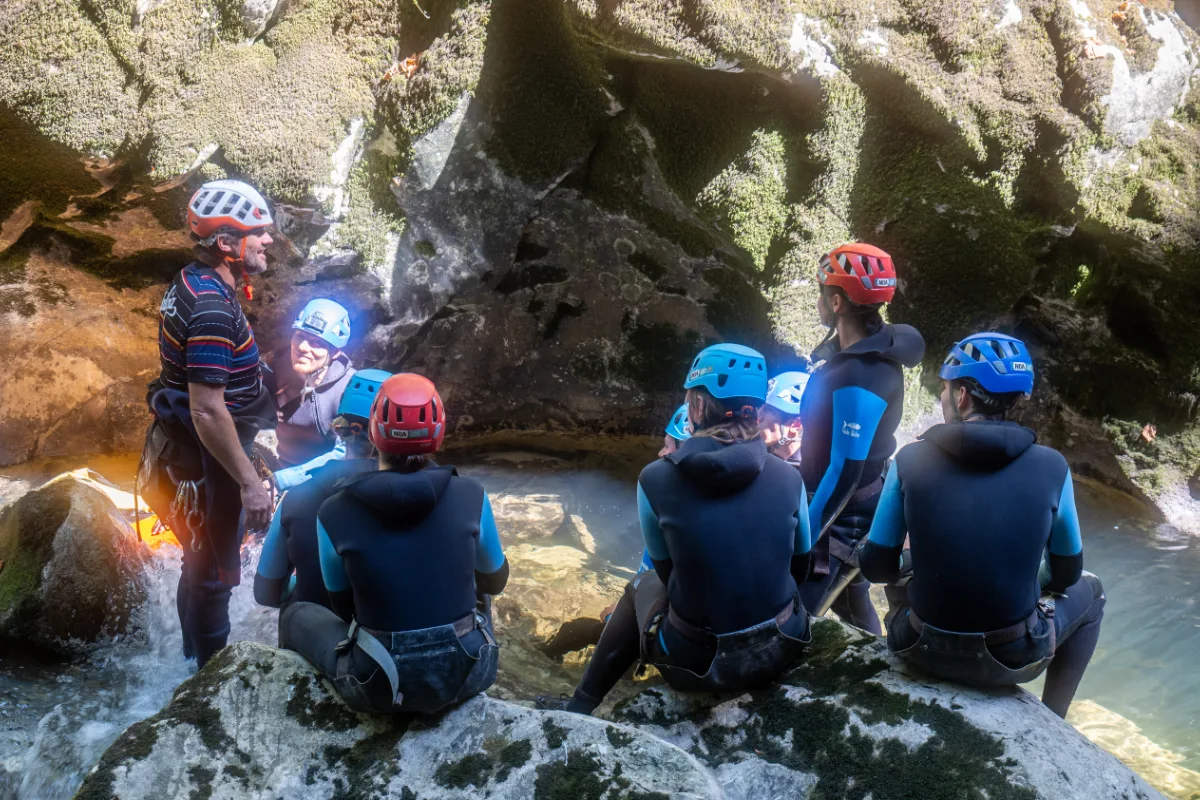 Guide de canyoning qui explique les consignes à son groupe au bord de la rivière dans un canyon du Jura