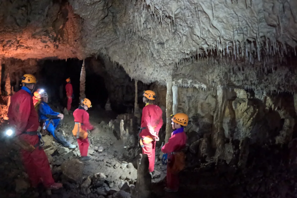 Groupe de spéléologues débutants avec casques et lampes frontales dans une grotte à concrétions du Jura