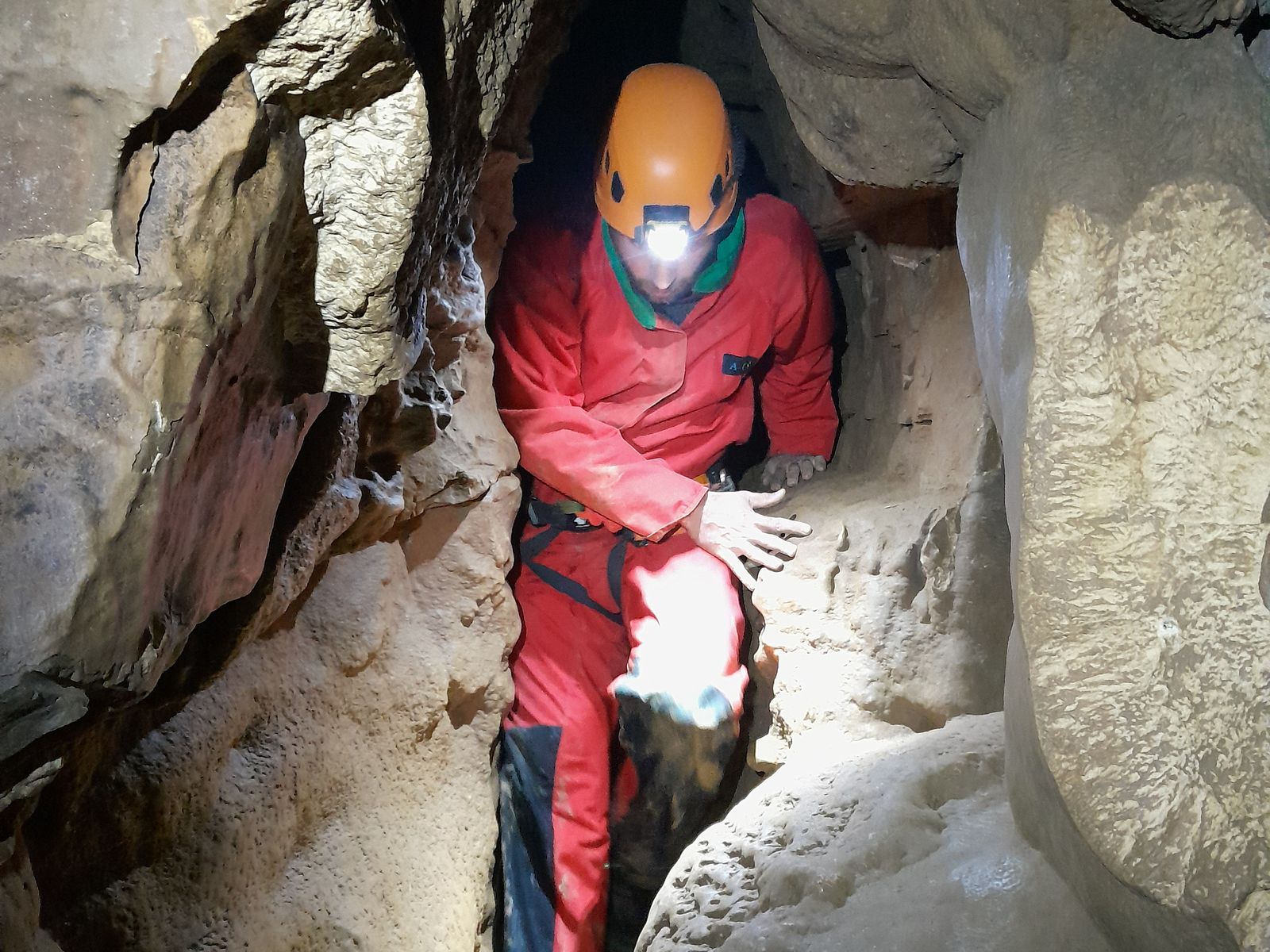 etroiture-speleologue-grotte-jura Spéléologue franchissant une étroiture entre deux parois calcaires dans une grotte du Jura