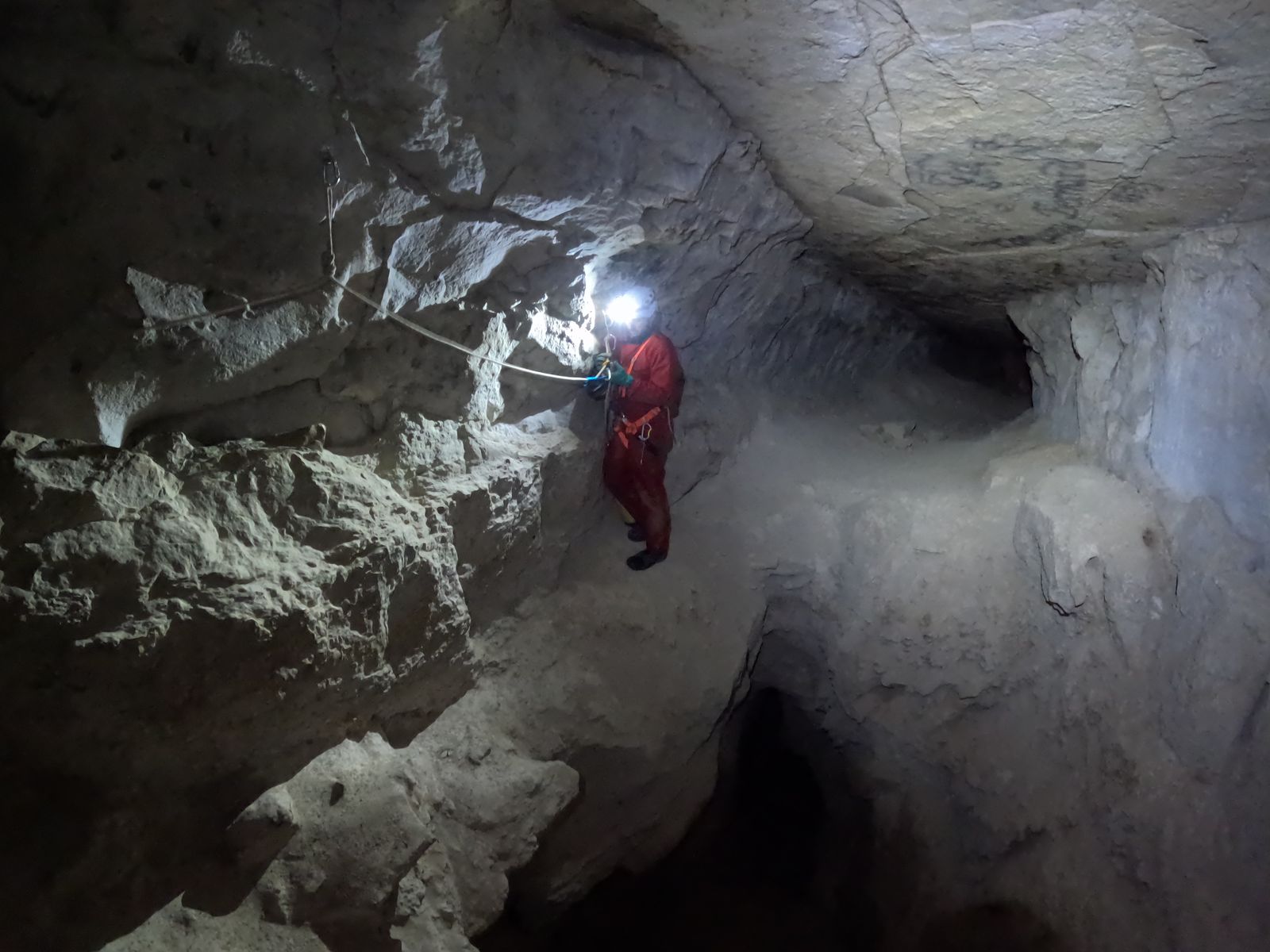 Spéléologue progressant à la lampe frontale dans une galerie calcaire de la grotte de Balerne