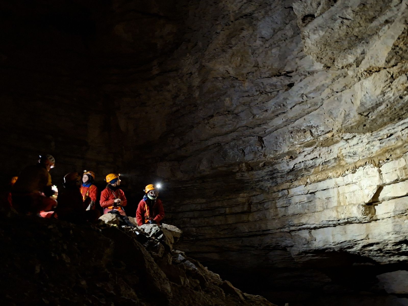 speleologues-salle-souterraine-gouffre Groupe de spéléologues à la lampe frontale dans une vaste salle souterraine aux parois stratifiées